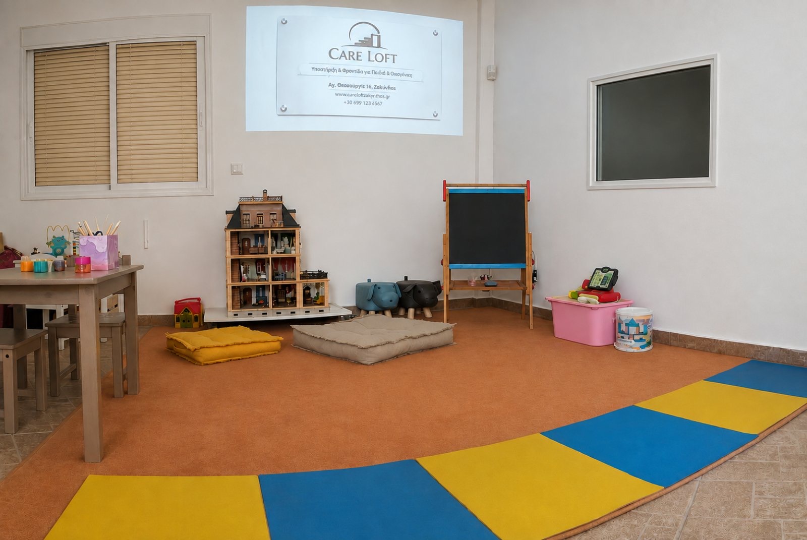 Ο χώρος πολλαπλών δραστηριοτήτων του Care Loft: παιδικό τραπέζι, κουκλόσπιτο, πίνακας ζωγραφικής, μαξιλάρια δαπέδου και μονόδρομος καθρέφτης παρατήρησης